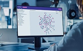 Ein Wissenschaftler sitzt an einem Schreibtisch und verwendet einen Computer, auf dessen Monitor die SYNTHIA™-Retrosynthese-Software angezeigt wird. Auf dem Bildschirm ist ein komplexes Netzwerk aus bunten Knoten und Verbindungen zu sehen, die synthetische Wege zu komplexen Molek&uuml;len darstellen. Die Softwareschnittstelle bietet M&ouml;glichkeiten zur Filterung und Analyse. Die Laborumgebung ist modern, und andere Wissenschaftler arbeiten im Hintergrund, was den kollaborativen und hochtechnologischen Charakter der Forschung unterstreicht.