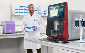 Smiling scientist sitting in front of bench with a microscope, CellASIC® ONIX2 live cell imaging system, and computer monitor