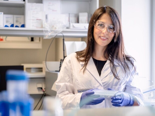 Eleni Samaridou stands in the lab wearing a lab coat, gloves and glasses.