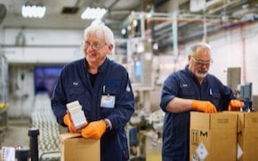 Two employees wear uniforms, gloves and safety glasses and package boxes. 