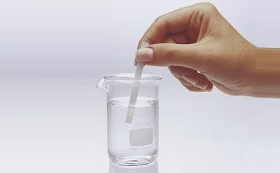 Chemist dips MQuant® test strip in a liquid contained in a small beaker to test a chemical parameter