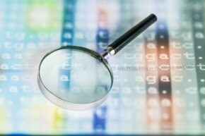 A magnifying glass sitting on top of a backlit display of genetic code showing ATCG genetic base code lettering